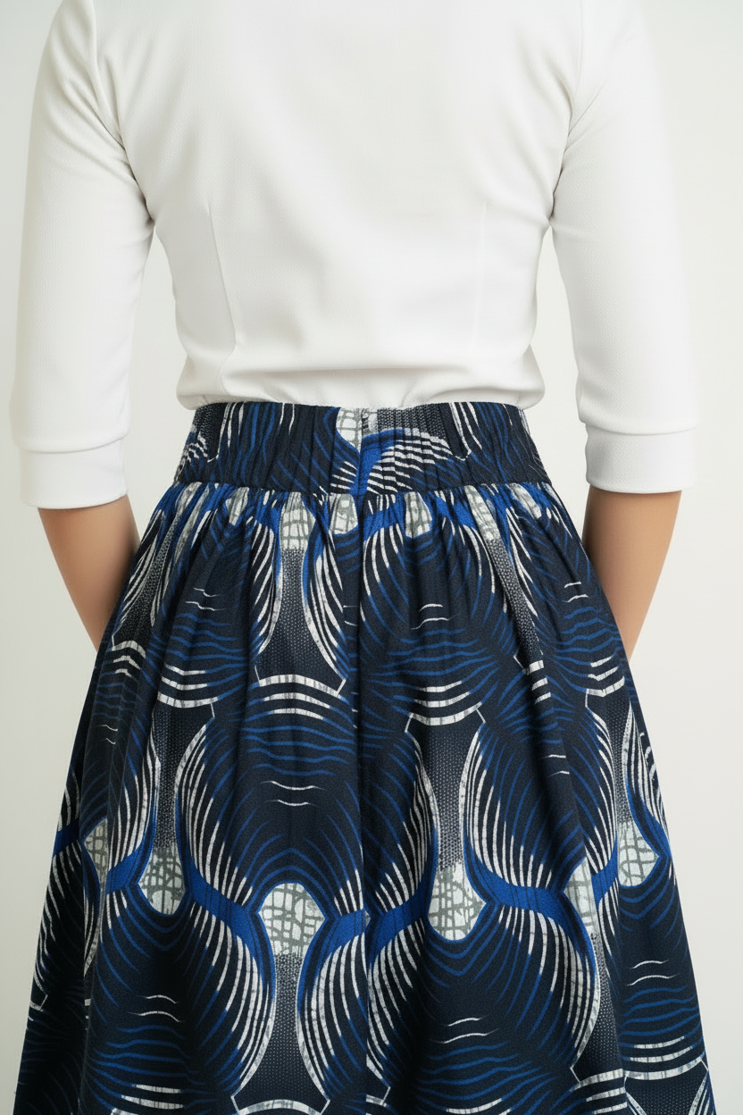 Person wearing a white top and navy blue patterned african ankara skirt on a light background